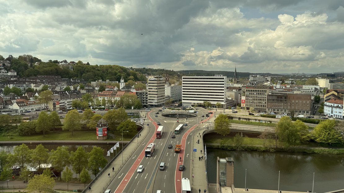 Luftaufnahme einer mehrspurigen Straße, die als Brücke einen Fluss überquert und in einen großen Kreisverkehr mündet.