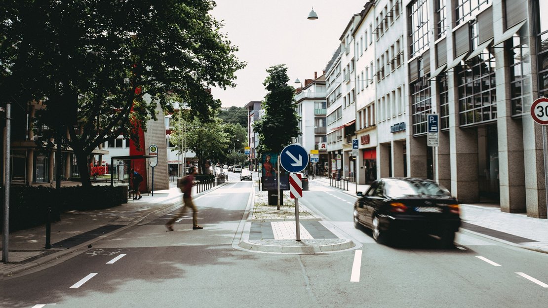 Eine innerstädtische Straße mit einem Fußgängerüberweg, der von einem Fußgänger überquert wird.